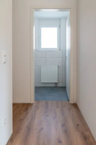 Blick vom Flur ins Gäste-WC mit Fenster und hellen Fliesen