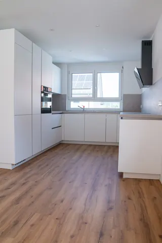 Weiße grifflose Einbauküche mit Hochschränken, Backofen und Fenster