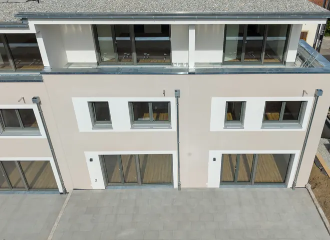 Zwei Häuser von der Gartenseite aus der Luft: gepflasterte Terrassen, Fensterband und Dachterrassen