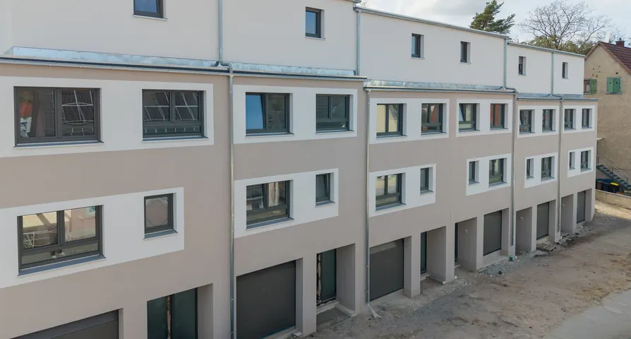 Die Hausreihe von der Straße: heller Putz mit weißen Fensterbändern, im Untergeschoss Garagentore und Eingangsnischen