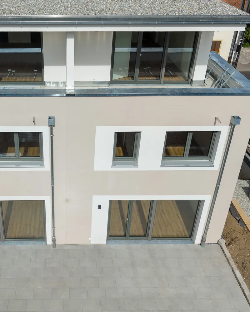 Ein Reihenhaus von der Gartenseite: gepflasterte Terrasse vor der Glasfront, darüber die Fenster des Obergeschosses und die überdachte Dachterrasse
